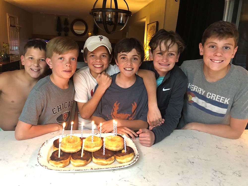 6 boys smiling in front of a plate of donuts with candles in them
