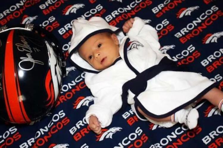 Baby Owen on a Denver Broncos blanket next to a Denver Broncos helmet