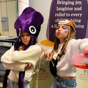 Two girls with face paint on looking at the camera with some silly attitude. One has a purple squid hat and folded arms and the other has a gorilla mask on her head and she is pointing at the camera with puckered lips