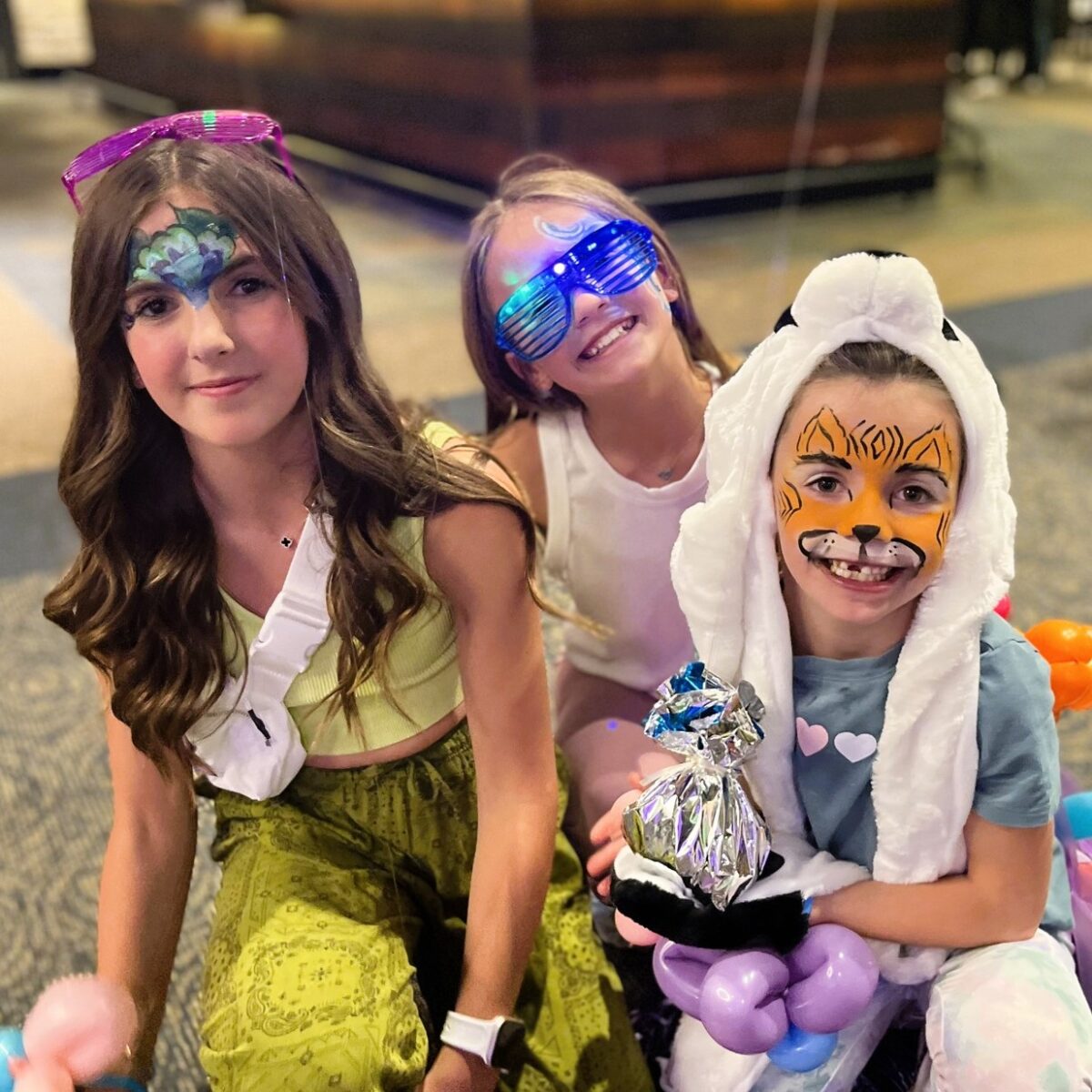 Three girls with face paint, silly hats, and slotted glasses smiling