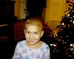 Gabby in her pajamas smiling with a Christmas tree in the background.