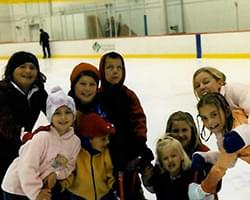 Gabby and a group of kids posing for a picture on the ice skating rink.