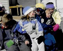 A group of kids with Gabby in their snow suites. They are sitting close to each other and talking.