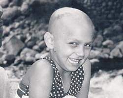 A black and white photo of Gabby with her mouth slightly open and smiling. She does not have much hair in the photo which shows this was after some of her treatments had started.