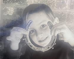 A black and white photo of Gabby. She is holding up a horse shoe with both hands and she is looking through it.