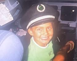 Gabby smiling with a pilot hat on. She appears to be in the cockpit of an airplane.