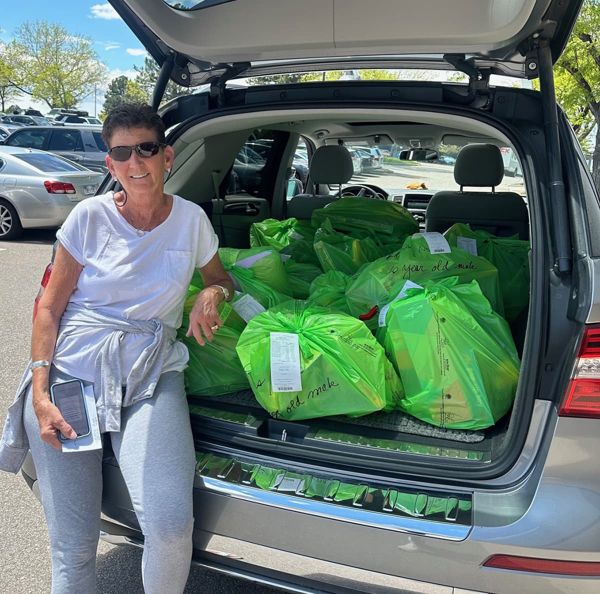 Susie Reynolds standing by the trunk of her car with lots of green grocery bags in the back.