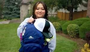 Teenage girl holding her Bag of Fun, that has a hat and bottle attached, outside in a residential yard.
